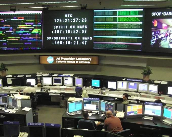 The mission control room at NASA's Jet Propulsion Laboratory, rows of monitors facing wall displays tracking spacecraft status.