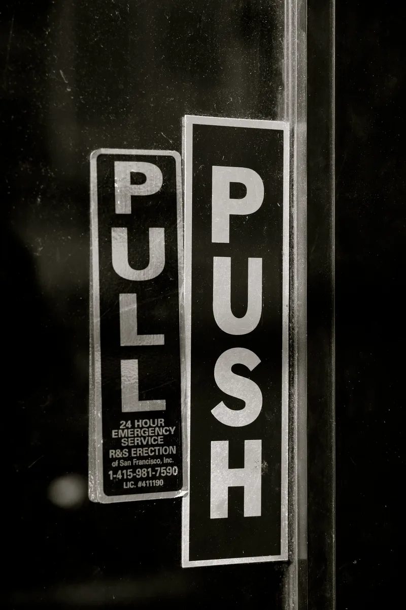 A dark glass door carrying both a PULL sign and a PUSH sign side by side, giving contradictory instructions for the same door.