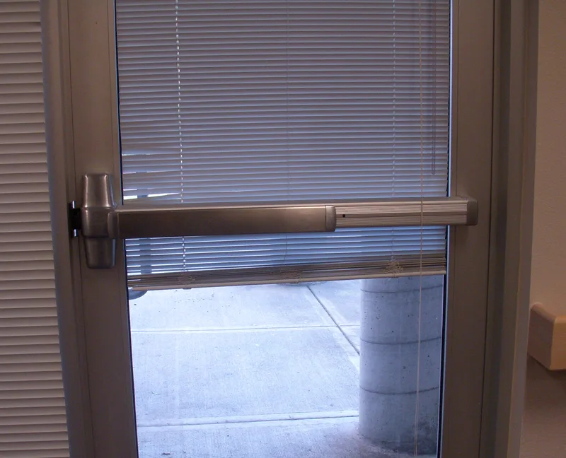 A horizontal panic bar spanning a glass exit door, with no plate or handle offering anything to pull.