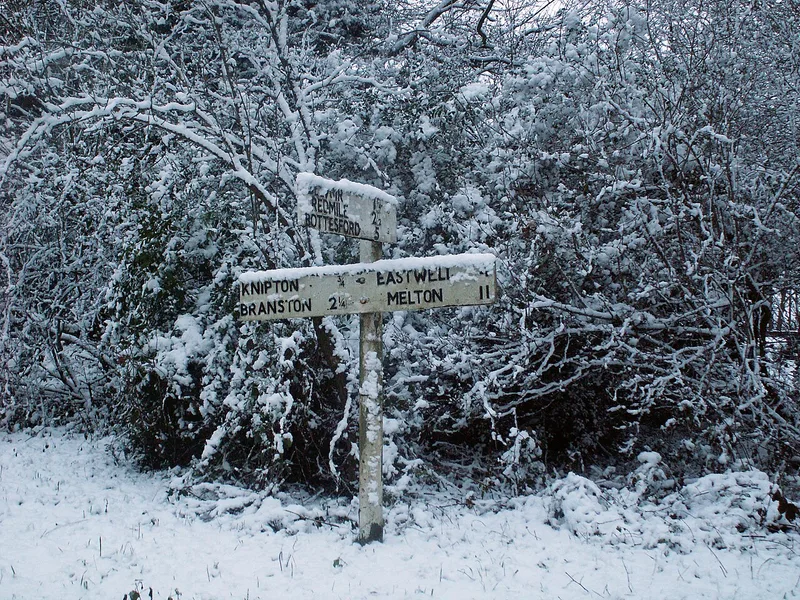A weathered wooden fingerpost signpost dusted with snow, pointing to villages including Knipton, Bottesford and Redmile in the Vale of Belvoir, Leicestershire.