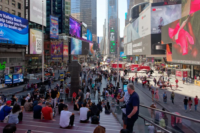 A crowd of tourists and visitors gathered in Times Square, New York City, beneath the billboards