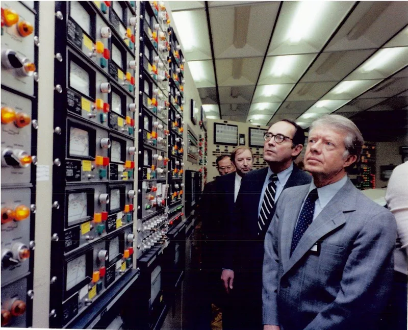 President Jimmy Carter and officials examine a wall of instrument panels covered edge to edge with rows of lit amber, red and green indicator lights inside the TMI-2 control room.