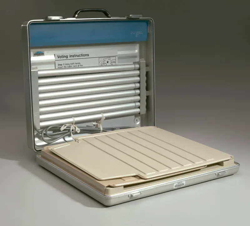 An open Votomatic vote recorder photographed against a plain background, showing its blank punch surface and instructional panel, with no screen or readout of any kind.