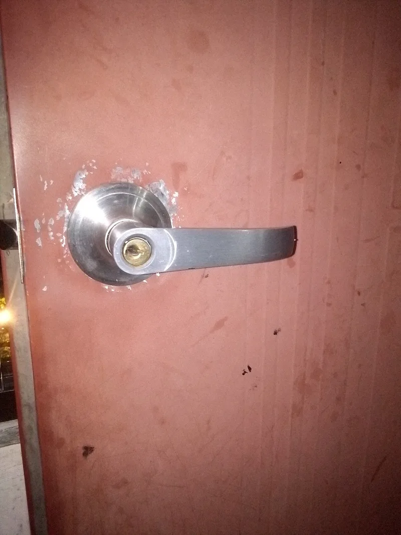 A lever door handle on a battered, grime-streaked door, with paint worn away in a ring around its base from years of hands finding the same spot.